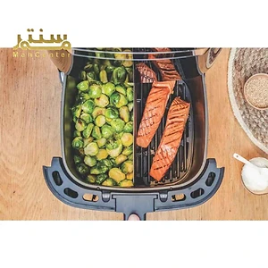 تصویر یک دستگاه سرخ‌کن بدون روغن با سبزیجات بروکلی و فیله ماهی سالمون درون آن است.