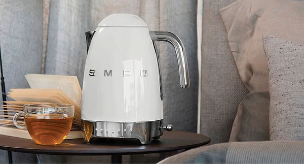 کتری برقی سفید با طراحی مدرن برند SMEG، قرار گرفته روی میز کنار فنجان چای