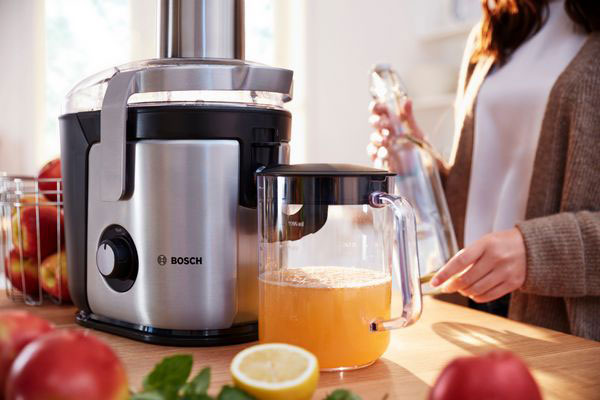 آبمیوهگیری bosch با طراحی مدرن در حال کار، همراه با پارچ پر از آب پرتقال تازه، در محیط آشپزخانه